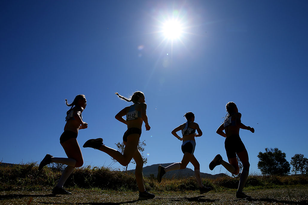 a group of girls running during cross country practice under a blue sky and a very bright sun