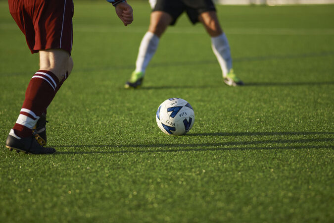 a close-up of artificial turf as two soccer players go for a soccer ball