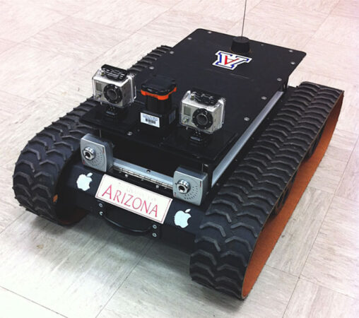 a photo of a small rectangular rover. It has treads on the long side of the rectangle. On the short side of the rectangle, facing the viewer, two cameras are mounted looking forward, they alost look like eyes. 