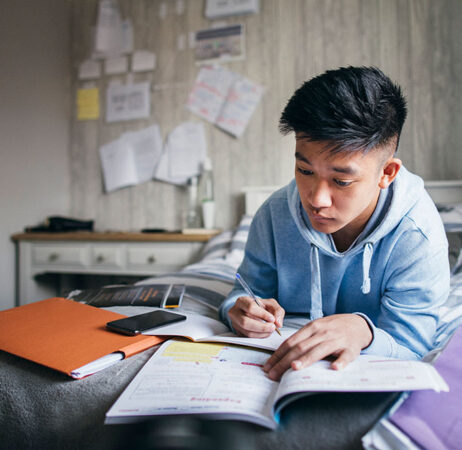 a photo of a young asian man studying his notes while lying in bed