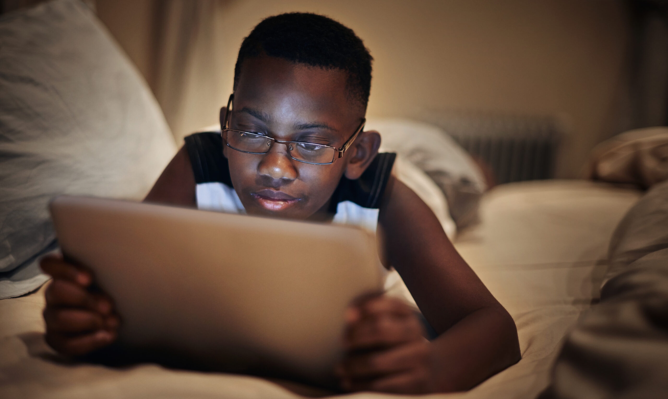 a boy lies on the couch while reading from a tablet screen