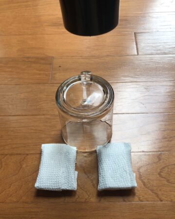 an upside down glass is placed on the floor; the rim of the glass holds the corners of two pieces of chocolate wrapped in paper towels, one dry and one wet; above, the tip of a hair dryer is pointed downward